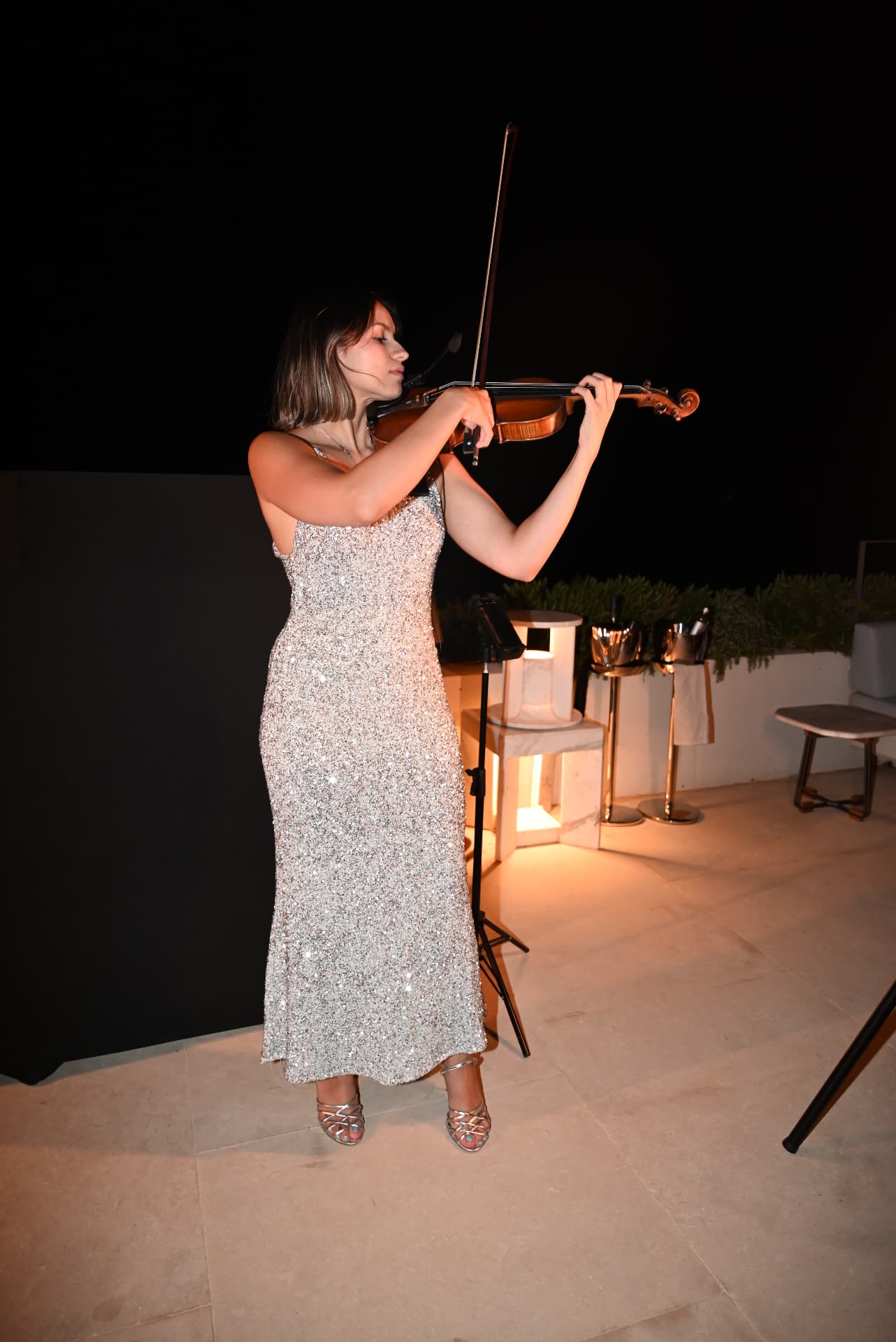 Violinist in a silver dress performing at night on a luxury terrace